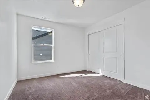 Bright room featuring a double-pane window, neutral wall paint, plush carpeting, and a built-in sliding closet with panel doors