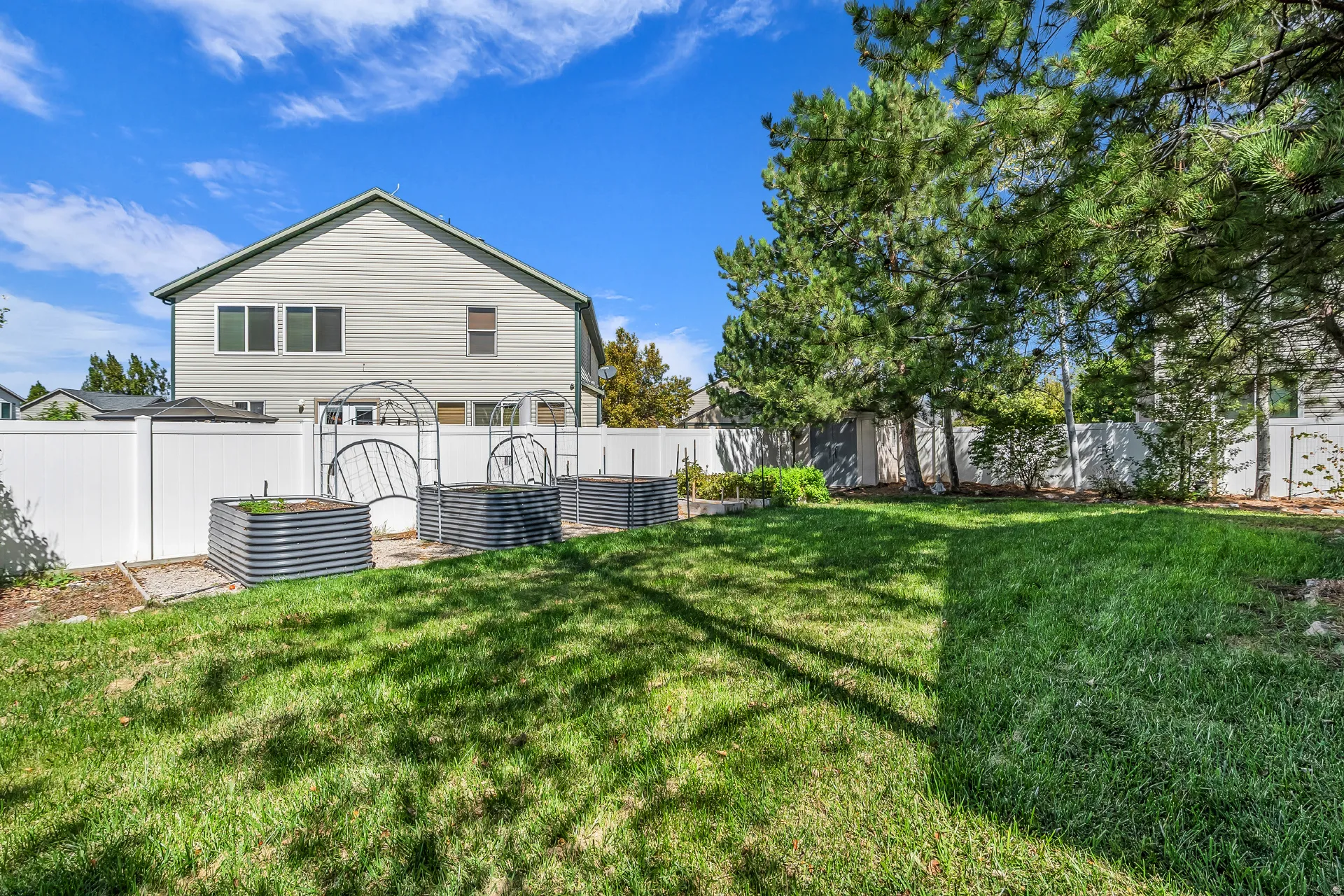 Expansive backyard with a manicured lawn, established trees, and a white privacy fence