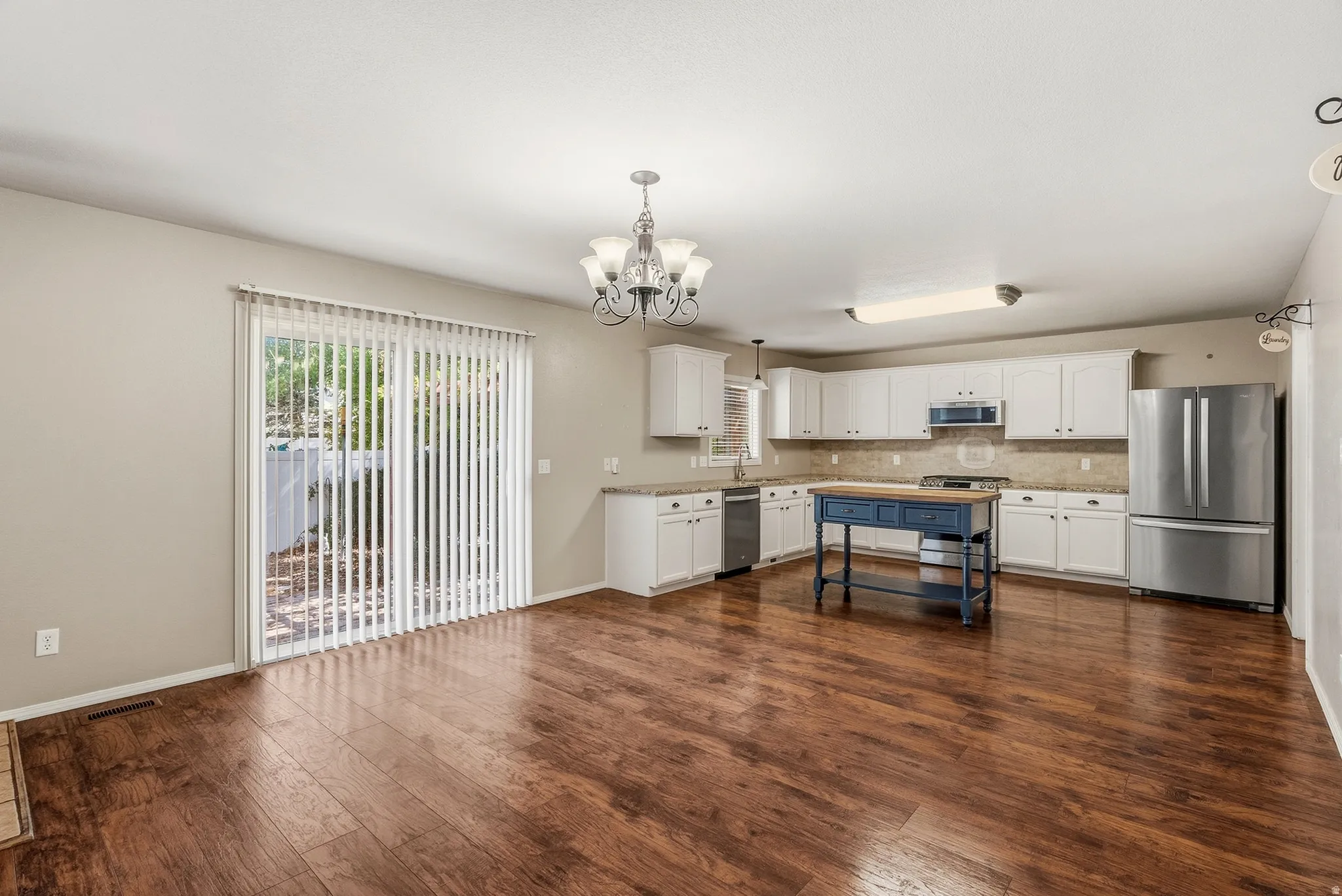 Spacious open-concept room featuring wood-finish flooring, white cabinetry, stainless steel appliances, and a glass sliding door