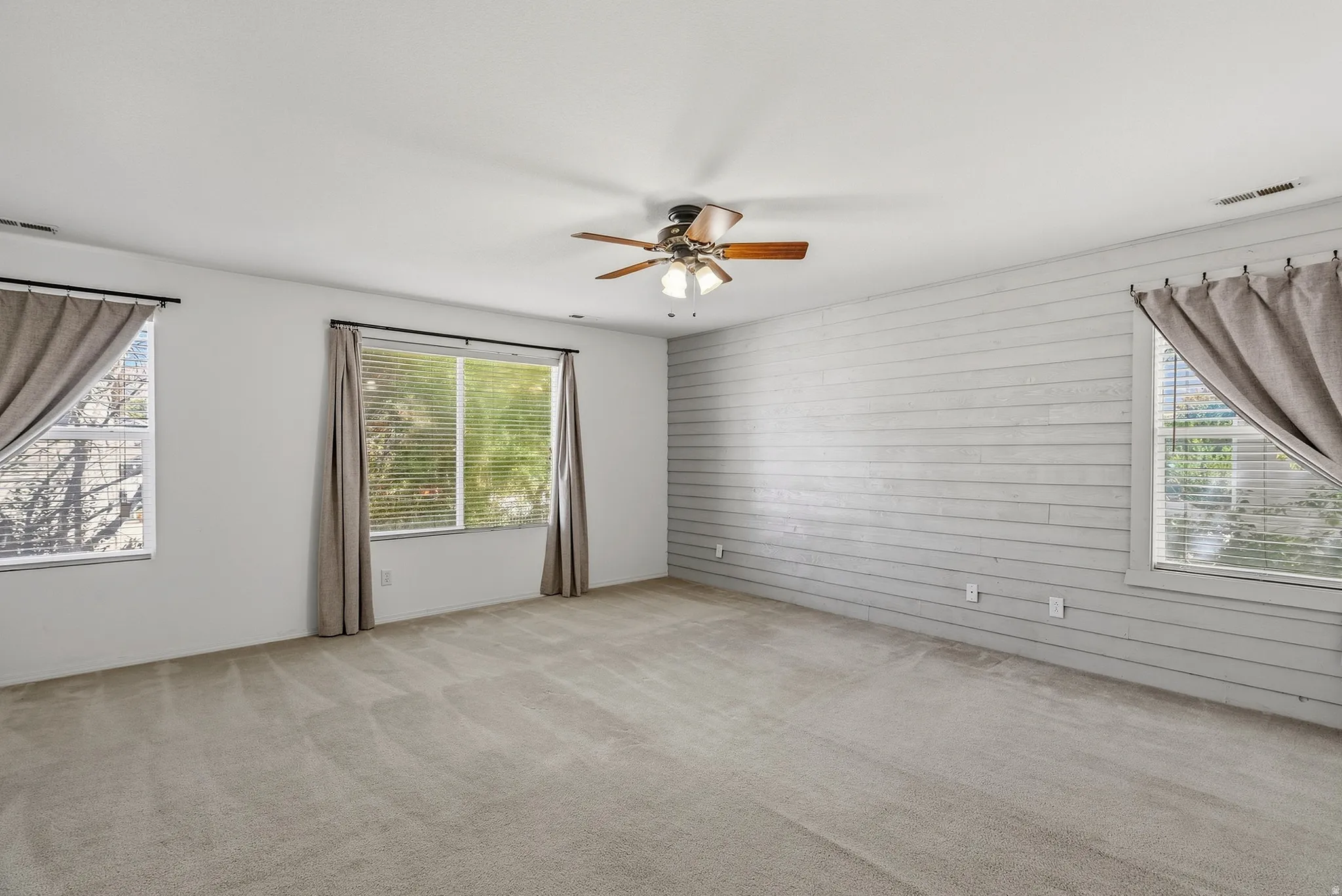 Expansive room with neutral carpeting, shiplap accent wall, multiple windows, and a ceiling fan