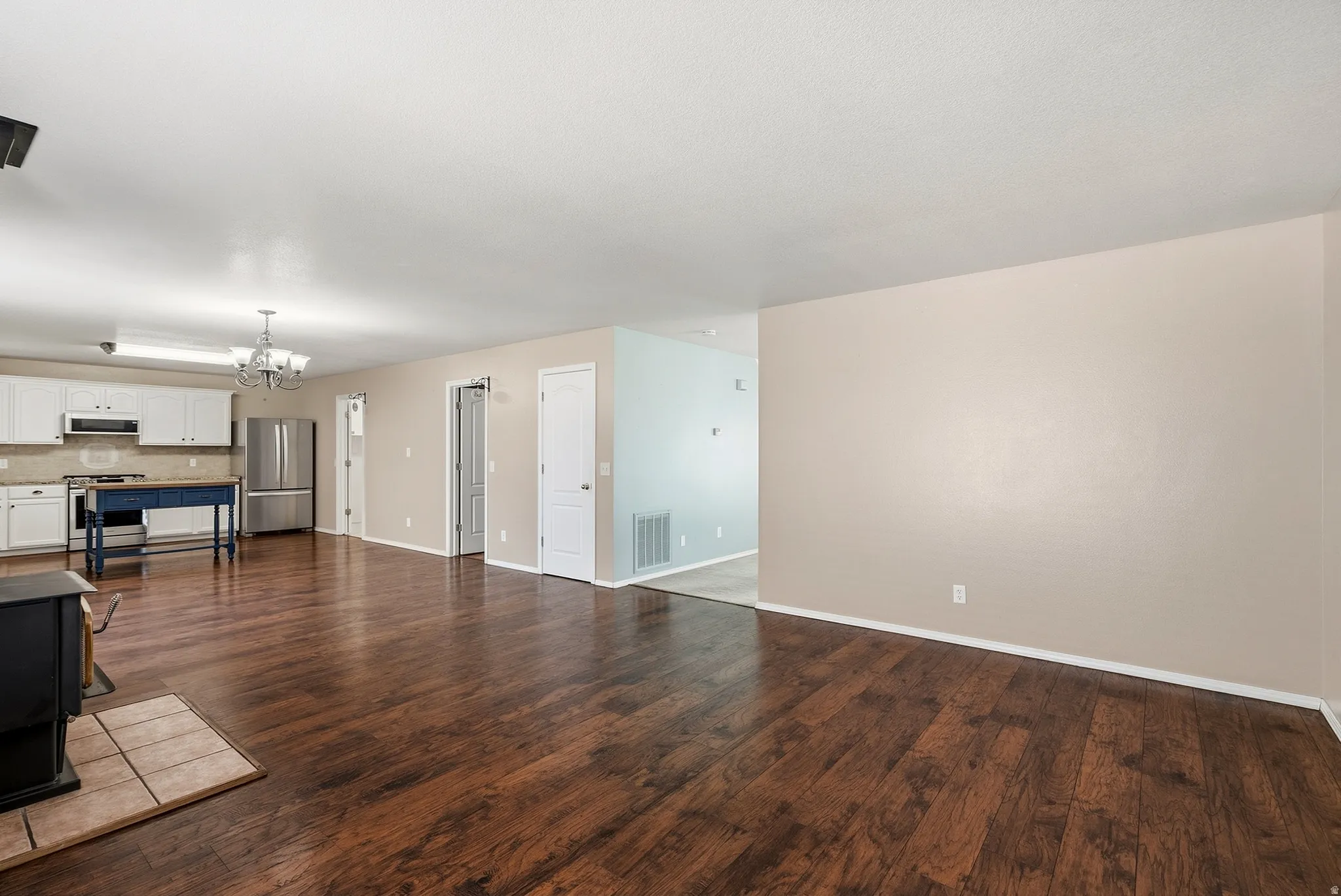 Expansive open-concept living area featuring wood-finish flooring, a kitchen with white cabinetry, and stainless steel appliances