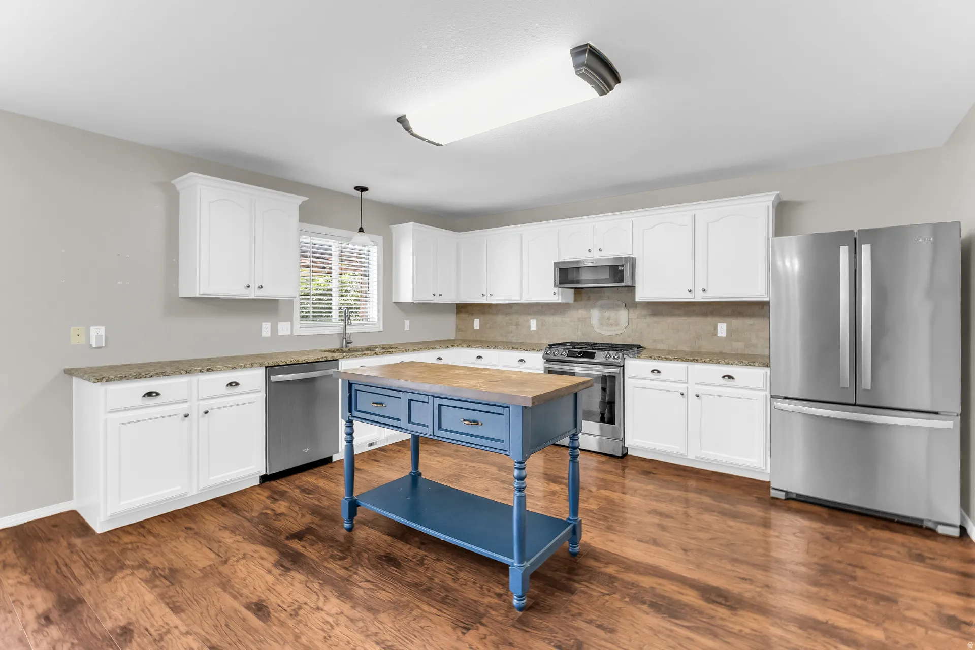 Kitchen featuring wood-finish flooring, white cabinetry, granite countertops, and stainless steel appliances