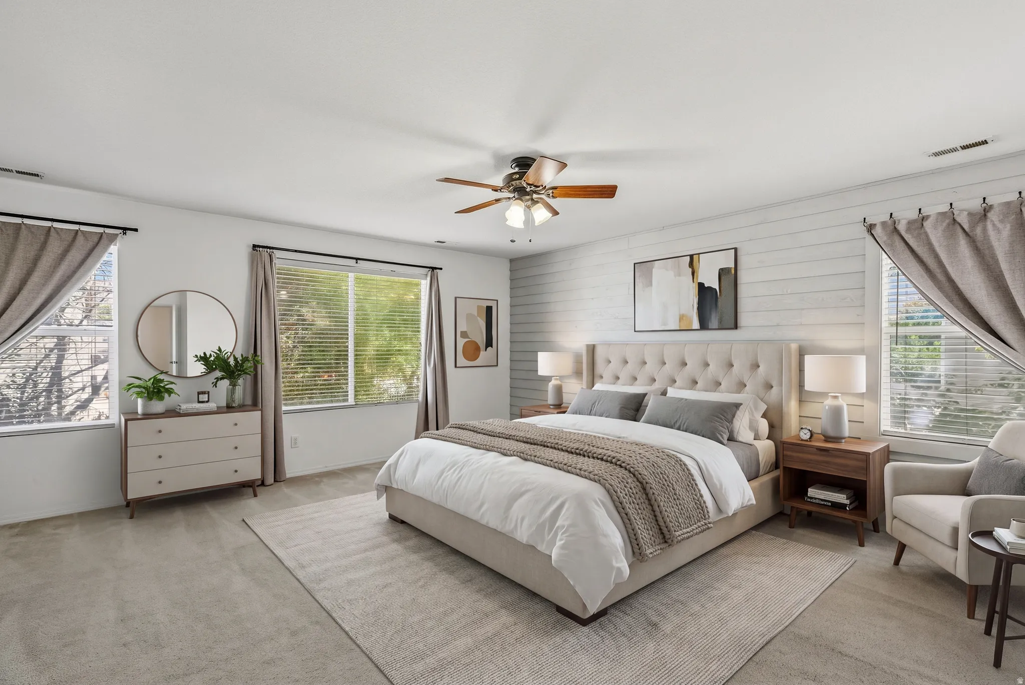 Carpeted flooring with a contrasting area rug, white textured accent wall, ceiling fan with integrated lighting, and multiple windows with blinds