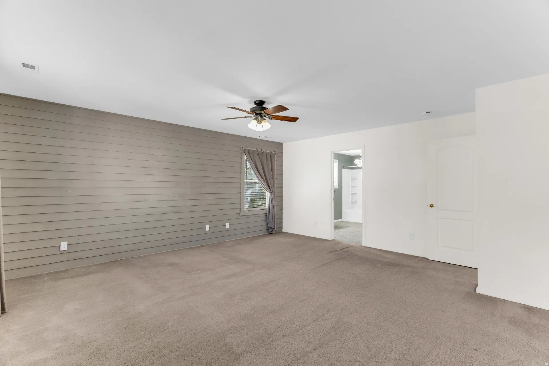 Expansive room with neutral carpet flooring and a wood-paneled accent wall