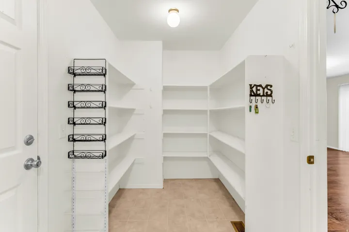 Spacious pantry featuring extensive built-in shelving, ceiling-mounted light fixture, and tiled flooring