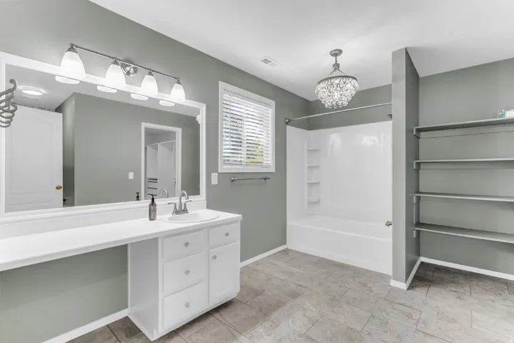 Bathroom featuring a single vanity with an integrated sink, a large wall-mounted mirror, a tub-shower combination, built-in shelving, and tile flooring