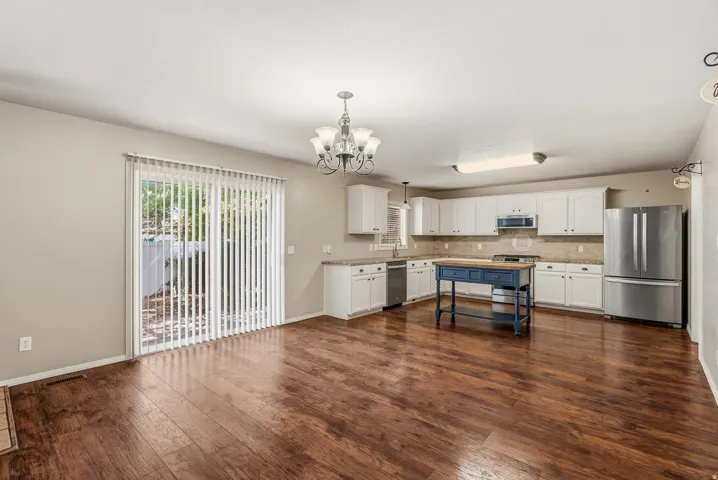 Spacious open-concept room featuring wood-finish flooring, white cabinetry, stainless steel appliances, and a glass sliding door