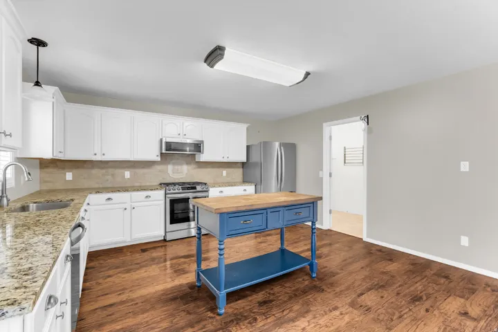 Kitchen featuring white cabinetry, stone countertops, wood-finish flooring, stainless steel appliances, and a tile backsplash
