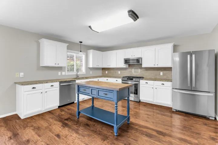 Kitchen featuring wood-finish flooring, white cabinetry, granite countertops, and stainless steel appliances