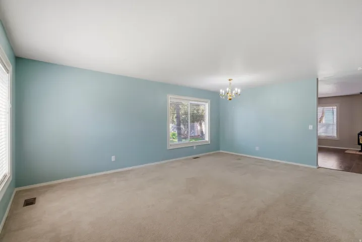 Expansive room with neutral carpeting, multiple windows providing natural illumination, and an overhead chandelier