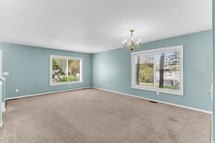 Spacious room with a neutral carpet flooring, light blue wall paint, and white trim