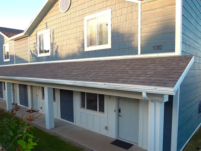 Multi-unit exterior with a covered entry, featuring asphalt shingle roofing, white gutters, and light blue siding