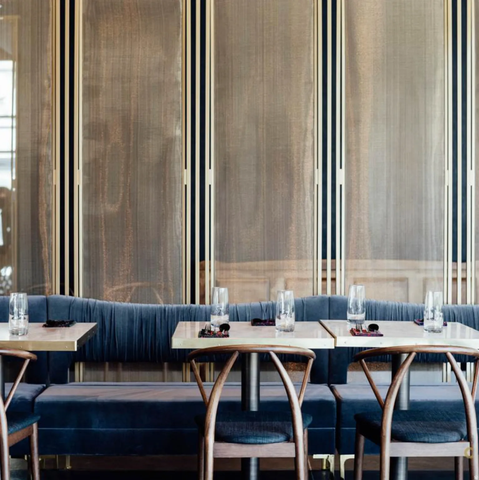 Banquette seating upholstered in deep blue velvet, complemented by a fluted wall paneling with vertical gold-toned accents
