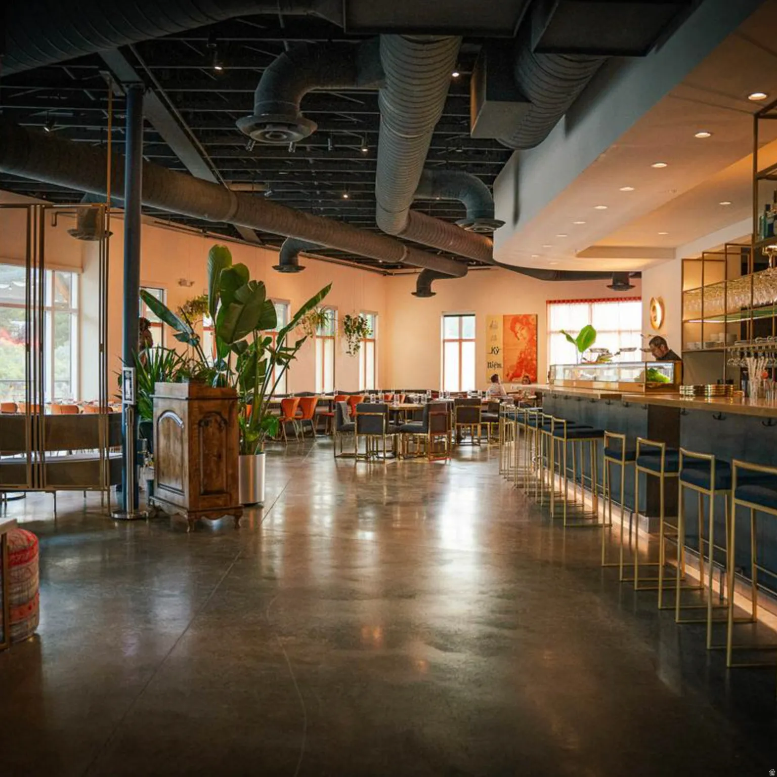 Spacious commercial interior featuring polished concrete flooring, exposed ductwork, a full-service bar, and multiple dining areas with abundant natural light