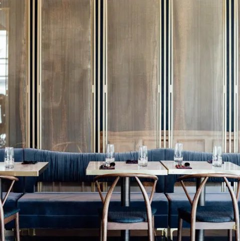 Banquette seating upholstered in deep blue velvet, complemented by a fluted wall paneling with vertical gold-toned accents