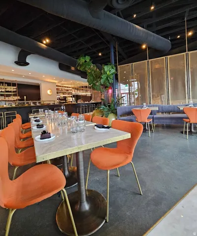 Expansive dining area featuring a polished concrete floor, exposed ceiling ducts, and a long marble-top table with gold-legged chairs