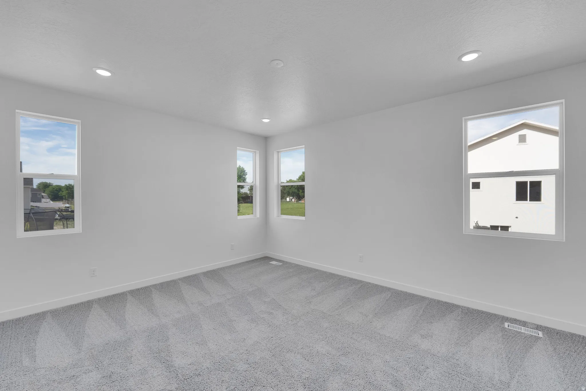 Spacious interior room featuring light gray patterned carpet, white walls, and multiple recessed ceiling lights