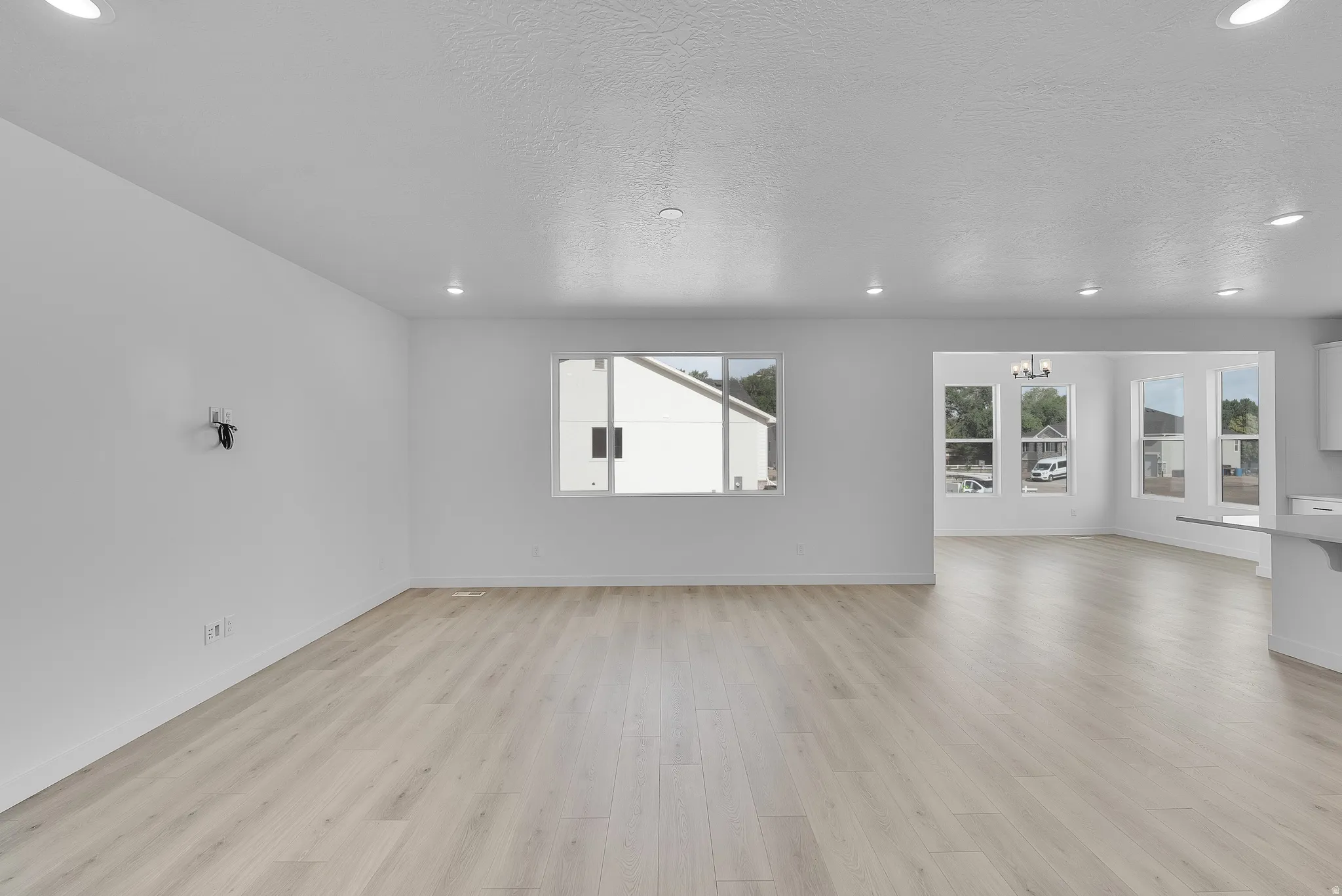 Spacious open concept living area featuring light wood-finish flooring, recessed ceiling lighting, and large windows providing natural illumination