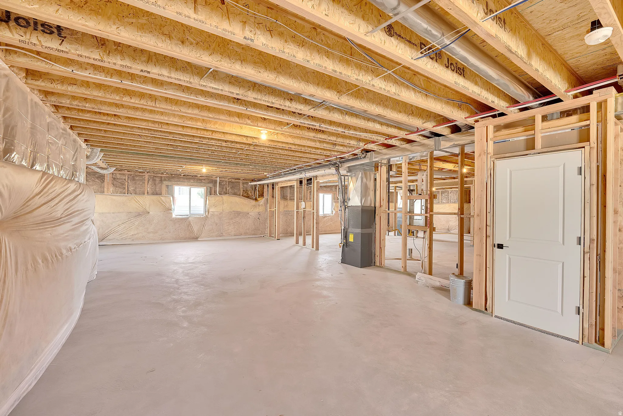 Unfinished basement with exposed ceiling joists, concrete flooring, framed interior walls, and multiple windows