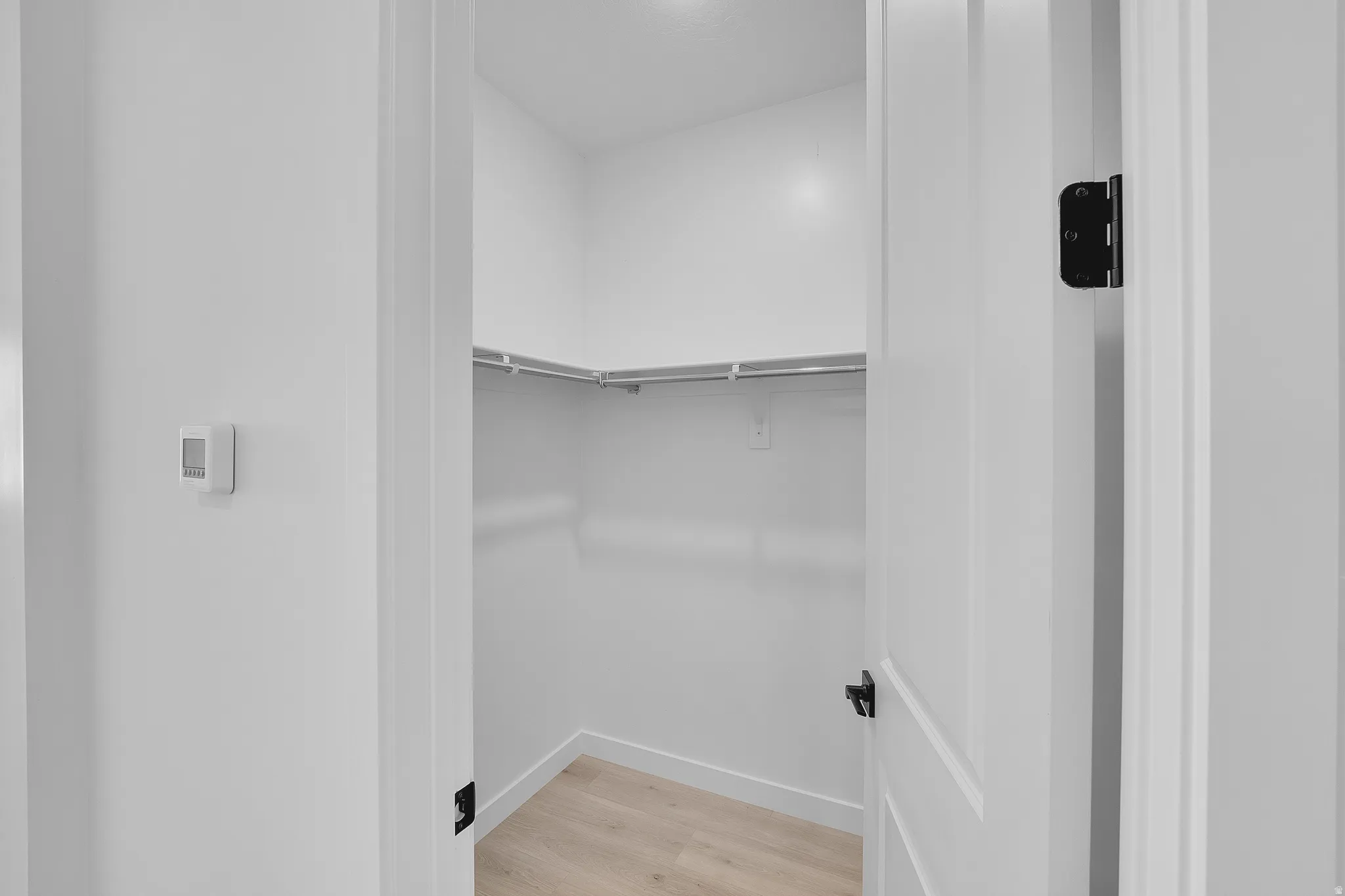 Recessed closet featuring wood-finish flooring, white walls, and built-in shelving and hanging rods