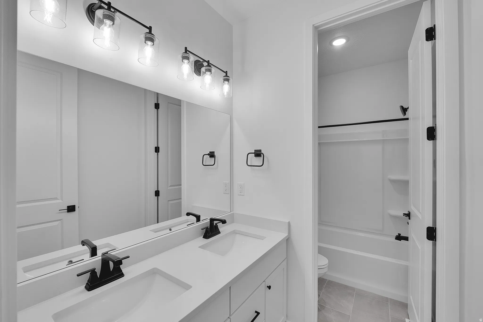 Bathroom featuring a dual vanity with undermount sinks, black hardware, and a large wall-mounted mirror