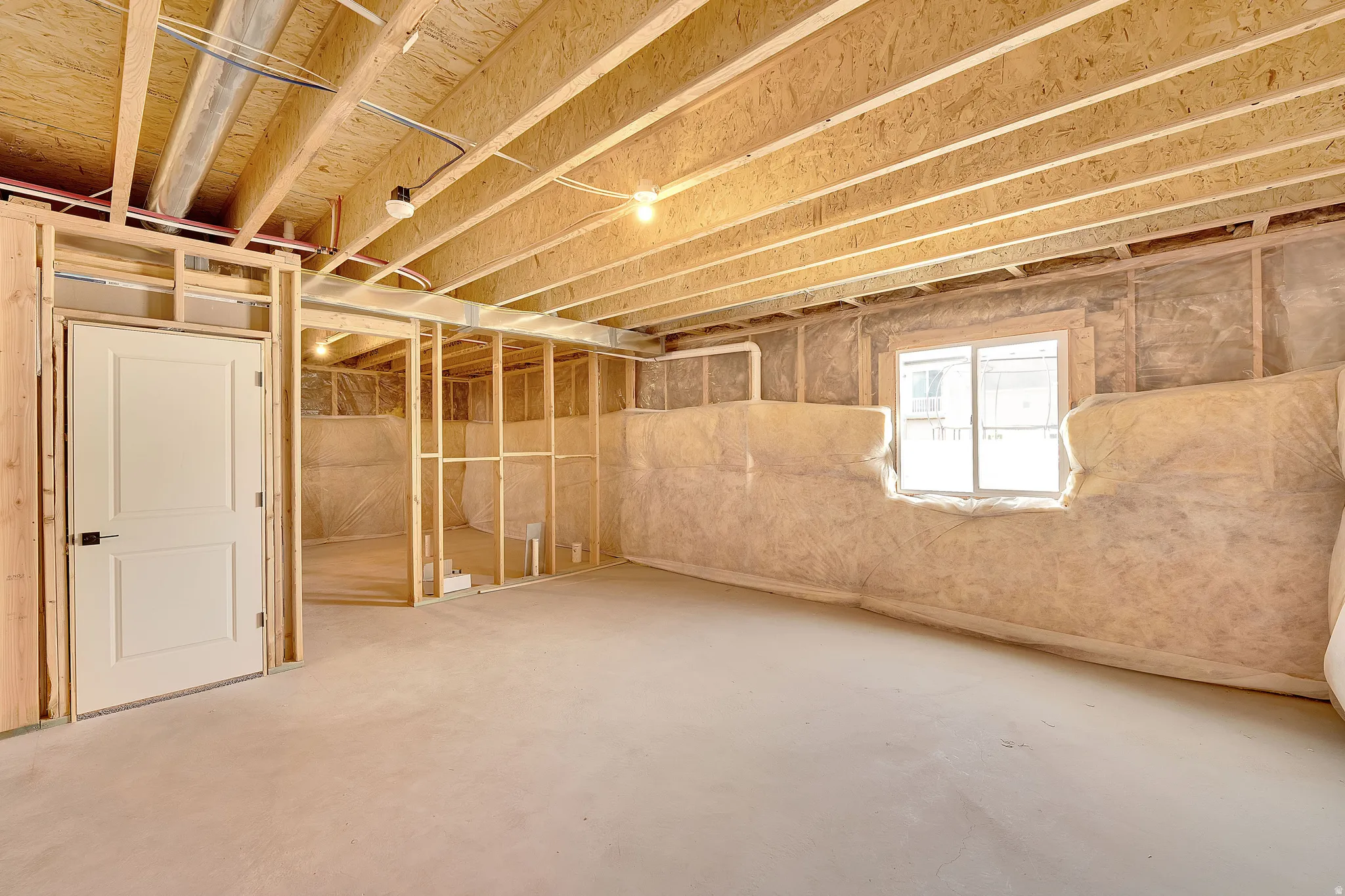 Unfinished basement featuring exposed wood joists, concrete flooring, framed interior walls, insulated exterior walls, and a window