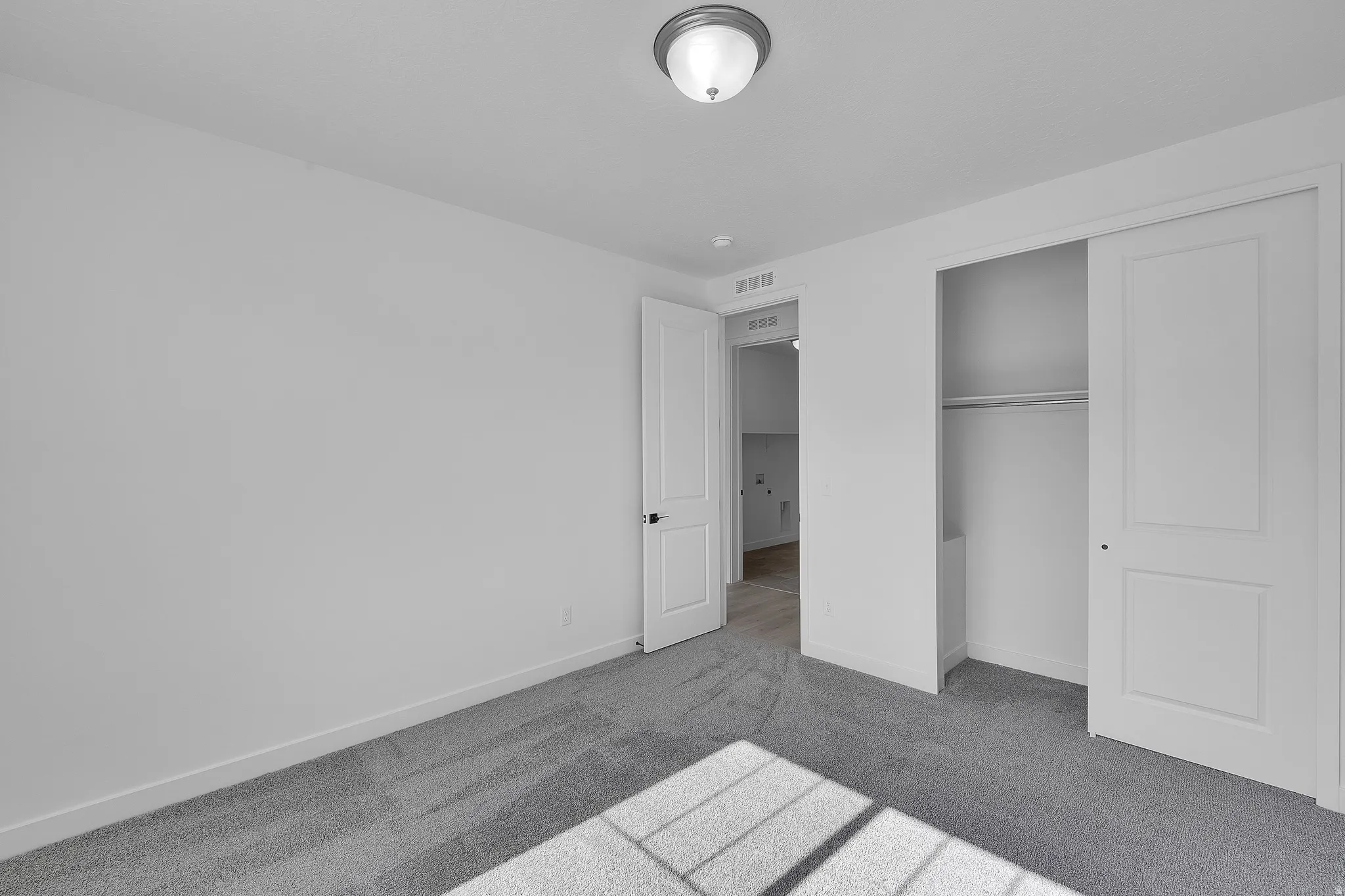 Carpeted room with white walls, a semi-flush mount ceiling light, and a closet with sliding panel doors