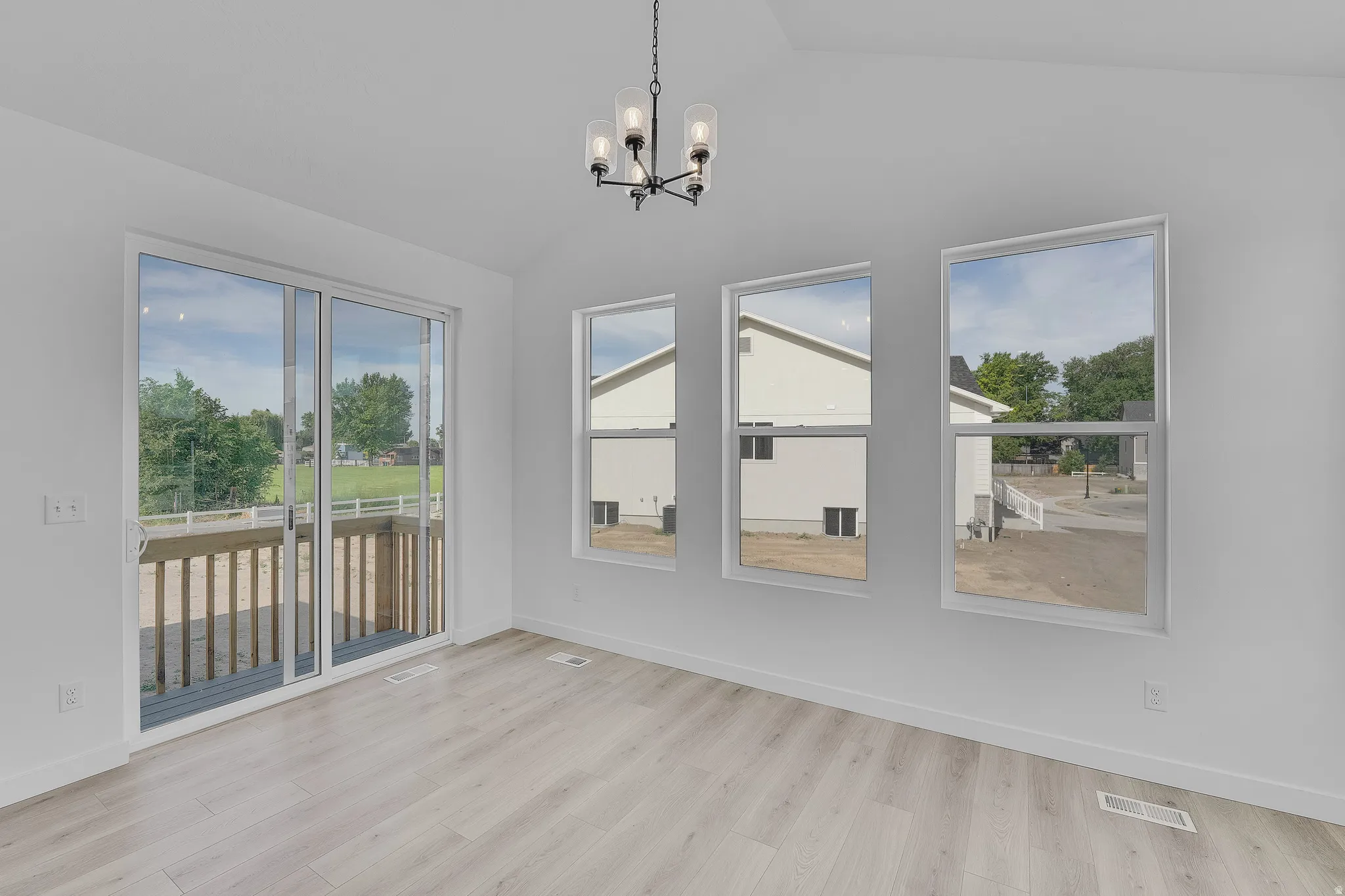 Spacious room featuring wood-finish flooring, a contemporary chandelier, multiple large windows, and a sliding glass door opening to a private deck