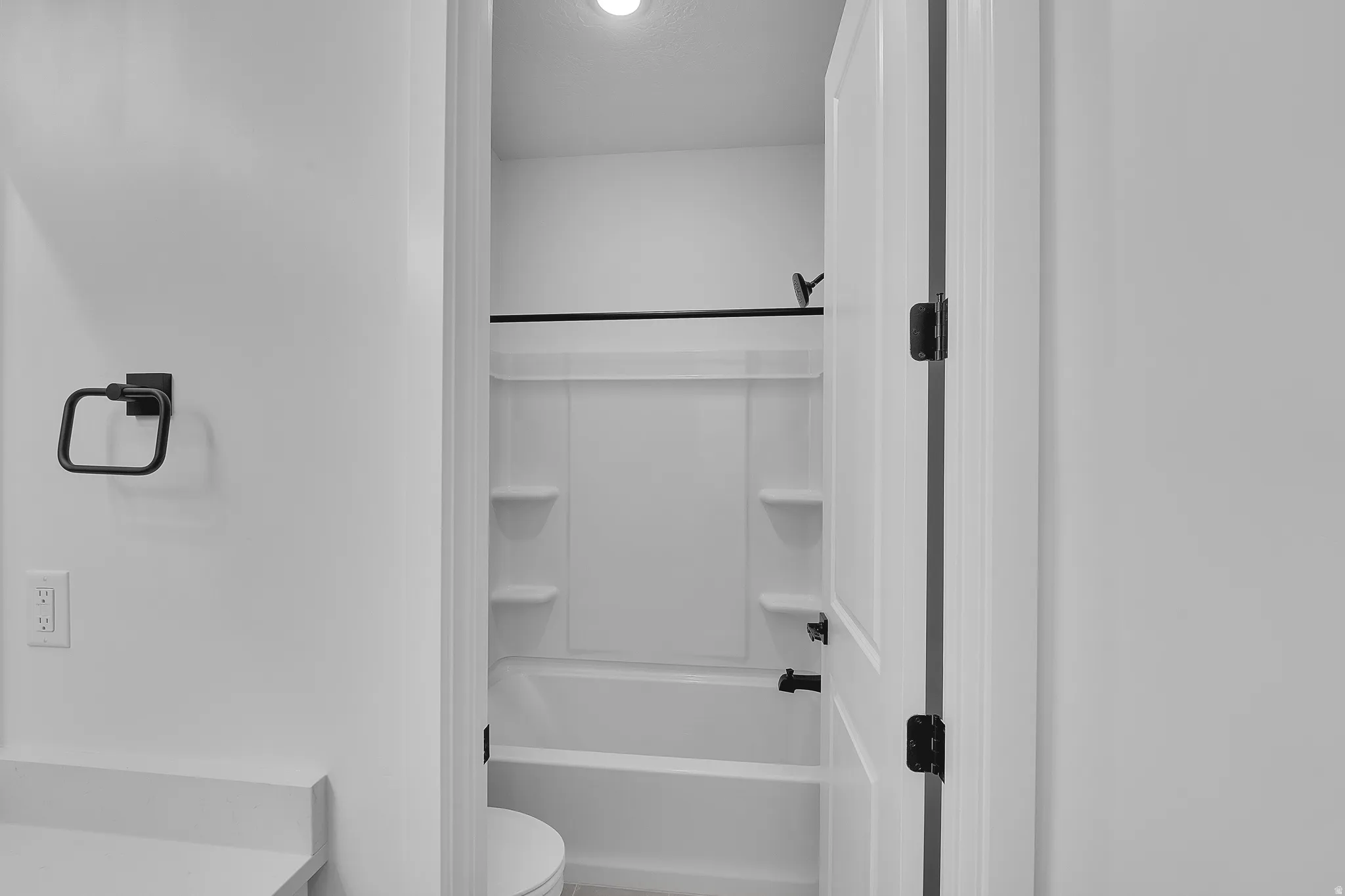 Bathroom featuring a white tub-shower combination with integrated shelving, matte black fixtures, and a coordinating towel ring
