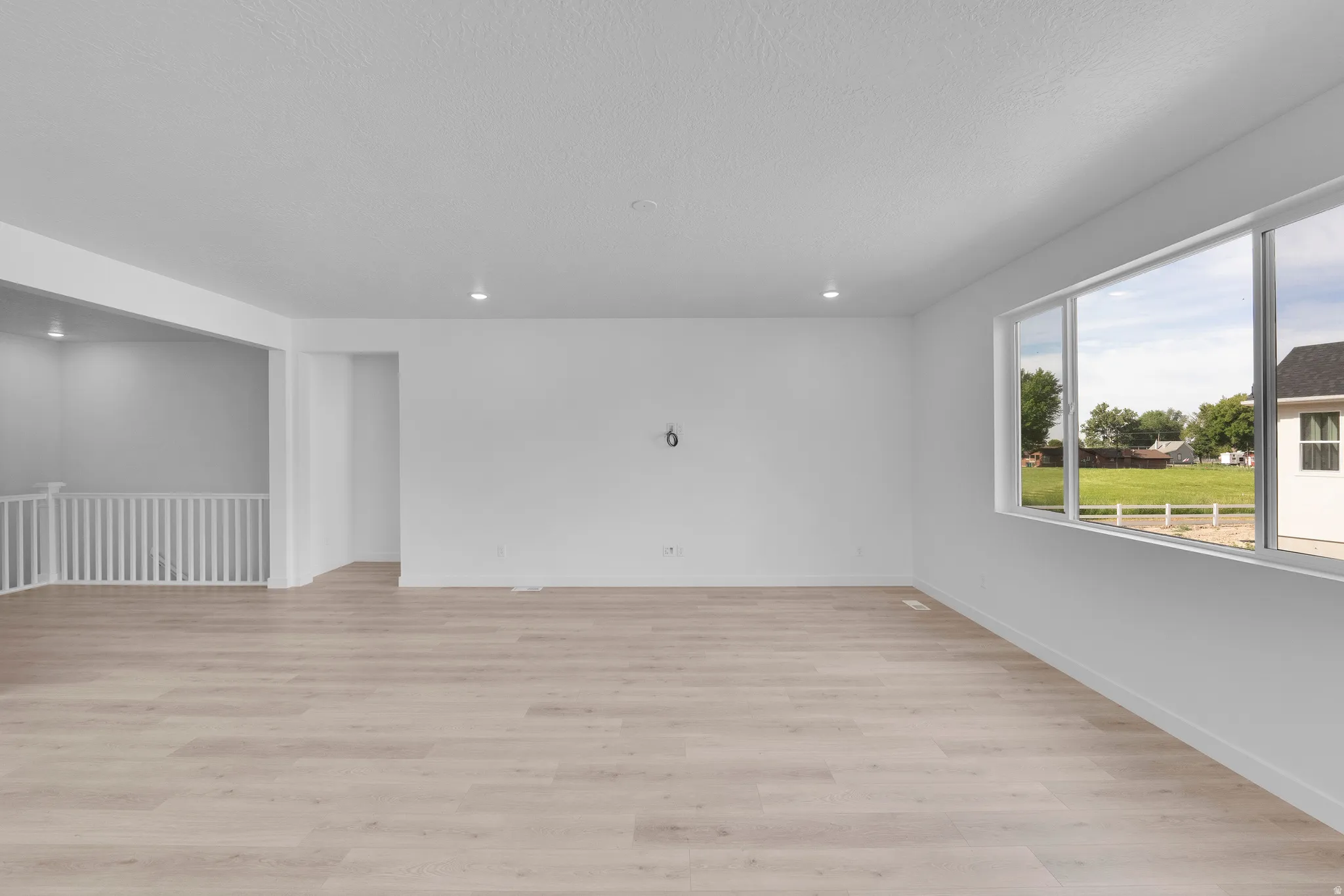 Spacious room featuring light wood-finish flooring, white walls, and recessed lighting