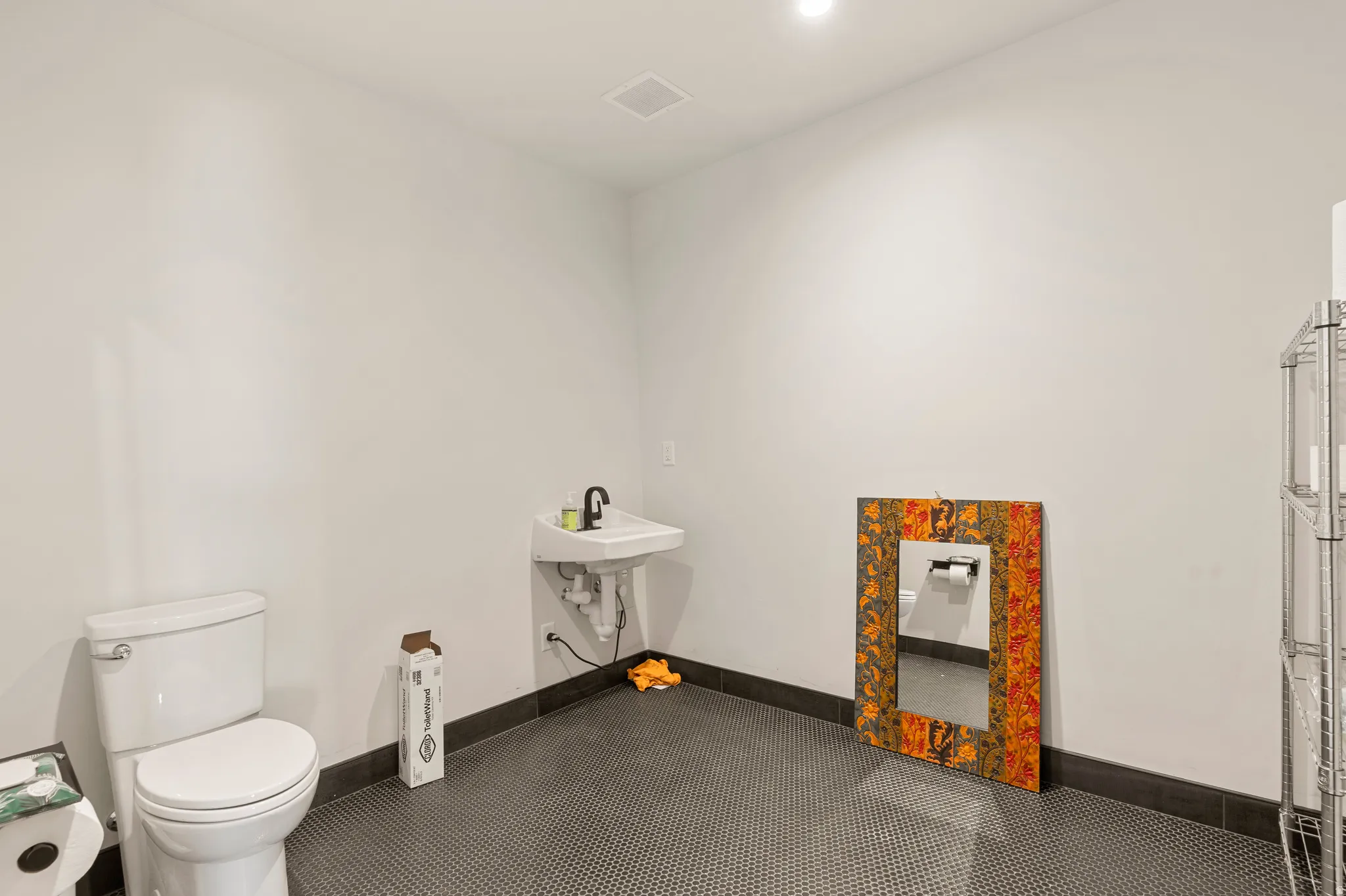 Restroom featuring a wall-mounted sink with a black faucet, white toilet, and dark mosaic tile flooring