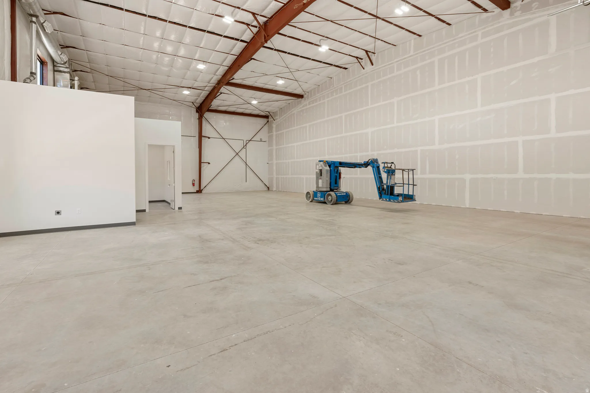 Spacious industrial interior featuring an open concrete floor, high ceilings with exposed metal trusses, and recessed lighting