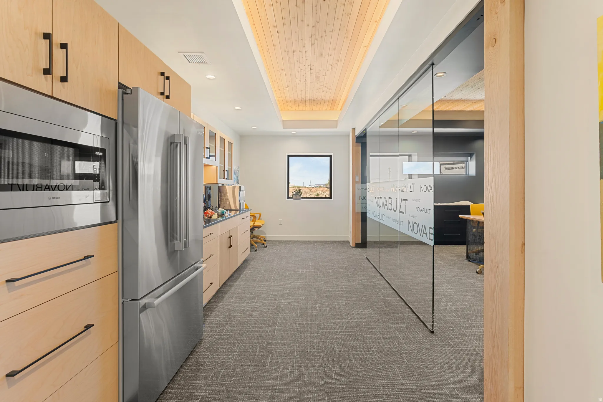 Contemporary kitchen area featuring light wood cabinetry, stainless steel appliances, and a wood-paneled ceiling treatment