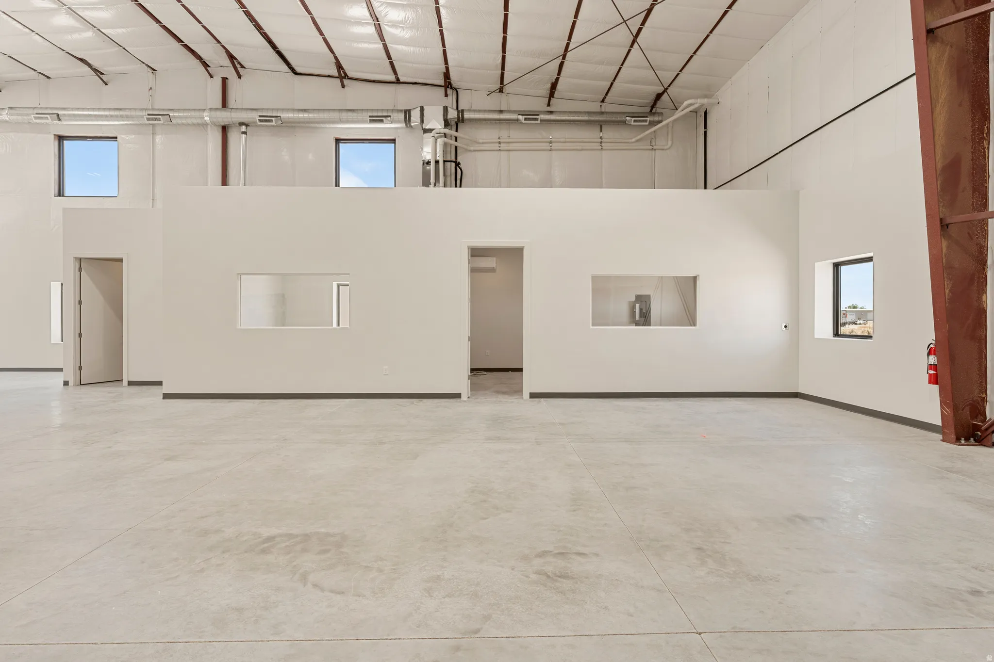 Expansive open-plan commercial space featuring concrete flooring, high ceilings with exposed ductwork, multiple windows, interior partitioning, and a second-story mezzanine with additional windows