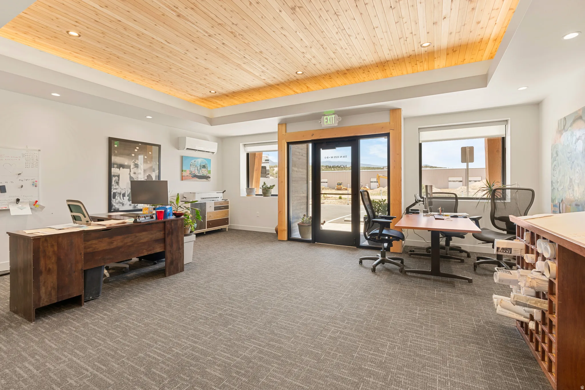 Open concept office space featuring a wood-panel ceiling with recessed lighting, carpet flooring, large windows, and a glass-paneled entry door