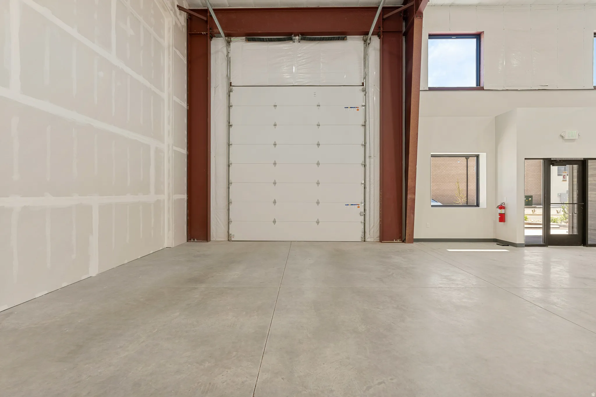 Spacious commercial interior featuring a large roll-up door, exposed structural beams, high ceilings, and concrete flooring