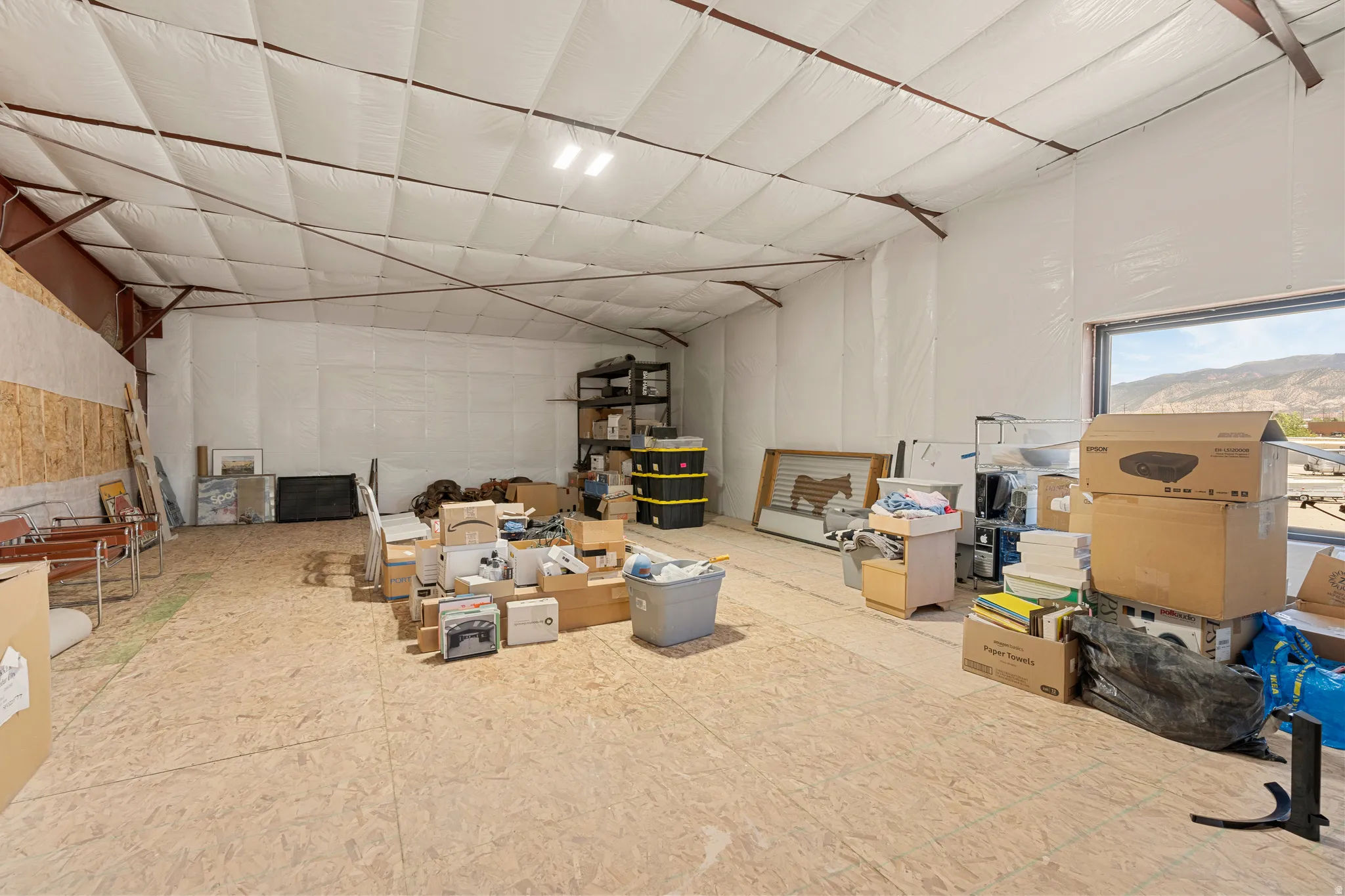Expansive interior space featuring a high ceiling with exposed structural beams, light-colored insulation, and a large window