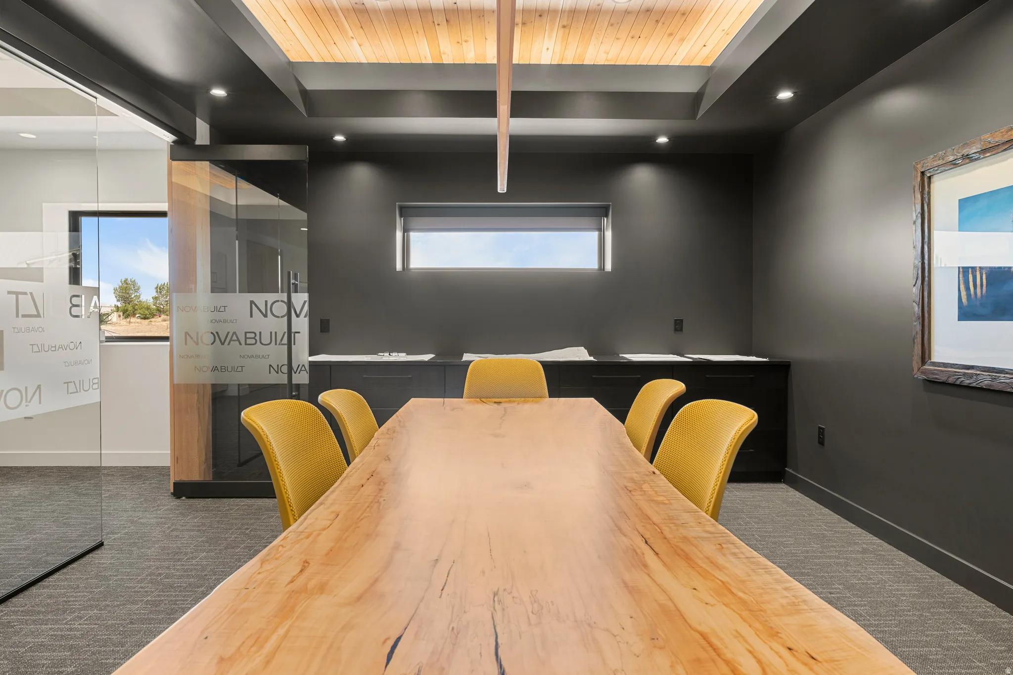 Conference room featuring a wood slab table, recessed lighting, wood-finish ceiling paneling, and an accent wall with a framed artwork