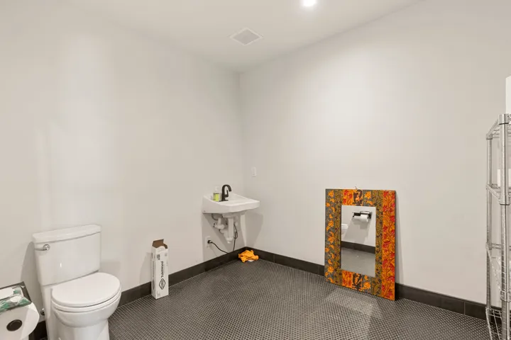 Restroom featuring a wall-mounted sink with a black faucet, white toilet, and dark mosaic tile flooring