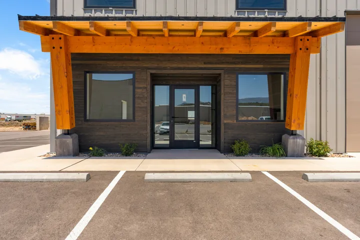 Modern commercial entrance featuring an exposed timber beam overhang, dark wood-finish siding, large windows, and a glass double-door entry