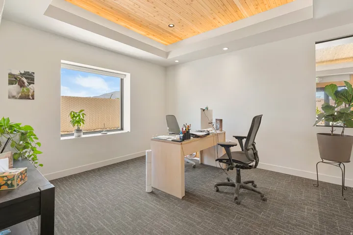 Recessed lighting illuminates the wood-paneled tray ceiling, complementing the white walls and patterned carpet flooring