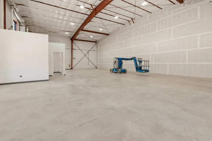 Spacious industrial interior featuring an open concrete floor, high ceilings with exposed metal trusses, and recessed lighting
