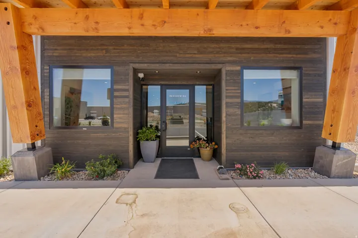 Modern building entrance featuring a glass door, two large windows, dark wood-finish siding, and exposed wood beams