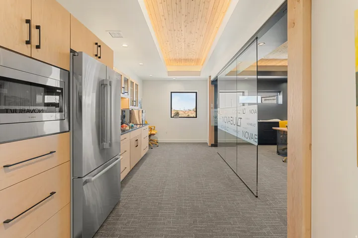 Contemporary kitchen area featuring light wood cabinetry, stainless steel appliances, and a wood-paneled ceiling treatment