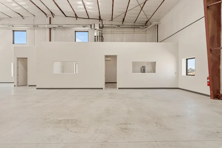 Expansive open-plan commercial space featuring concrete flooring, high ceilings with exposed ductwork, multiple windows, interior partitioning, and a second-story mezzanine with additional windows