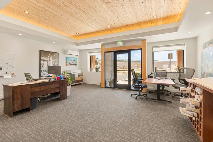 Open concept office space featuring a wood-panel ceiling with recessed lighting, carpet flooring, large windows, and a glass-paneled entry door