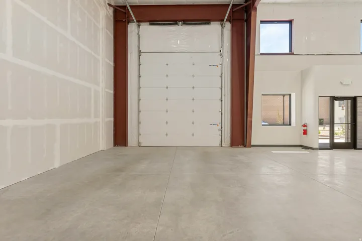 Spacious commercial interior featuring a large roll-up door, exposed structural beams, high ceilings, and concrete flooring