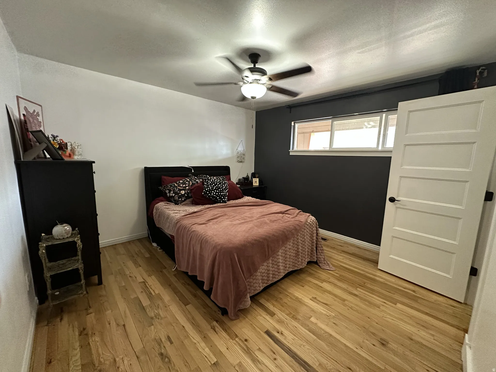 Wood-finish flooring, ceiling fan with integrated lighting, horizontal windows, and a panel-style interior door