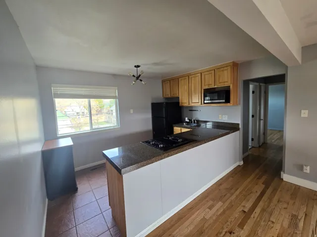 Kitchen area featuring wood cabinetry, black appliances, a built-in cooktop, and a granite-finish countertop