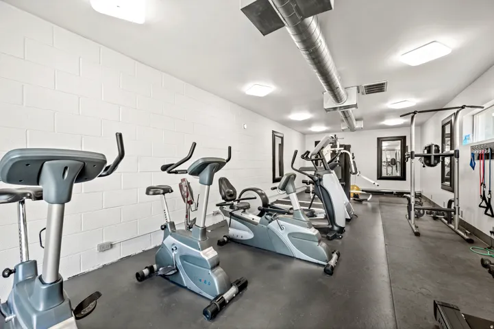 Dedicated fitness area featuring white block walls, exposed ductwork, recessed lighting, and dark rubber flooring